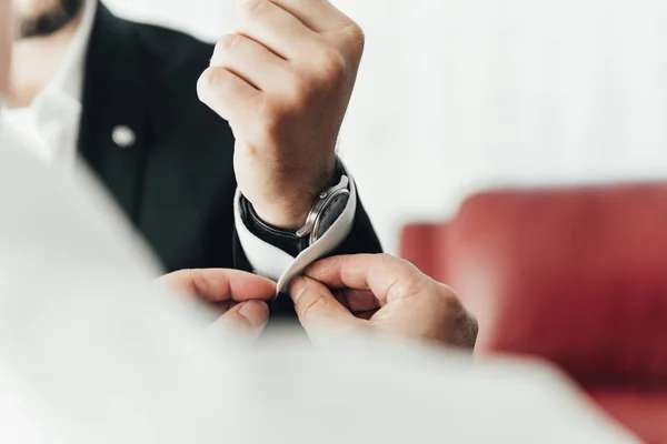 Close-up of fashion image of man\'s luxury watch on wrist. Businessman in black suit with watch on hand. Fastening a wristwatch. Body detail of a business man. Man\'s hand in a white shirt