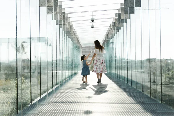 Young family walking inside the modern building in high-tech architecture style. Mom with little daughter walking, playing and having fun. Mother\'s day concept. Always happy together