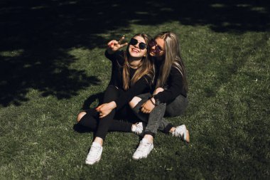 Gülen kızlar eğleniyor ve yeşil çayırda dinlensinler. Komik genç yaz tatili zevk ve yeşil çim üzerinde yalan. Güzel genç kadınlar parkta dışında yaz günlerini harcama