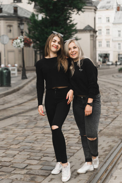 Happy friends having fun walking in city center. Beautiful young positive girls spend summer holidays. Two smiling pretty teenagers travel around old wonderful European city. Joint vacation concept