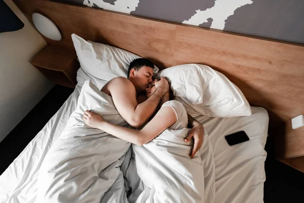 Young couple in hotel. Family waking up in the morning on bed. Cute couple waking up after a night sleep. Happy couple flirting and speaking in the morning on a comfortable bed at home. Relaxing after morning sex. Feets on bed