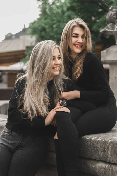 噴水に座っている2人の美しい女の子 噴水の近くで遊ぶ黒い服を着た友人 若い観光客が旧市街で話し 笑っている 夏休みを楽しむポジティブな女性 — ストック写真