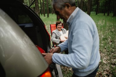 Yaşlılar araç bagajını açar. Yeni arabalarına sahip yaşlılar. Mutlu ve güzel yaşlı insanlar. Büyükbaba ve Büyükanne araba yakınında doğada birlikte stand.