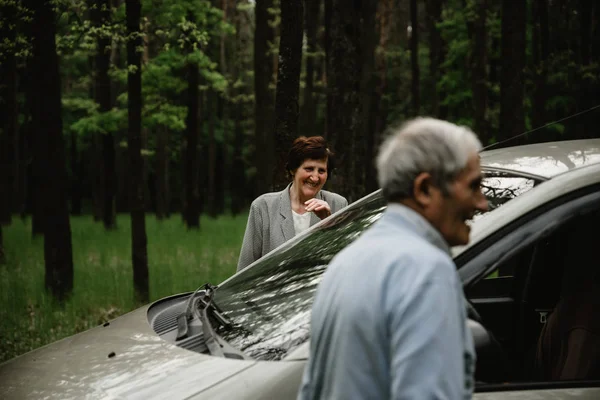 Grandpa and grandmother stand together on the nature near the car. Old couple having fun on the nature. Seniors with their new car. Happy and beautiful old people