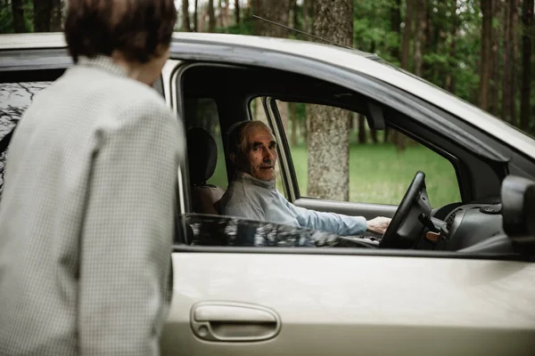 Grandpa and grandmother stand together on the nature near the car. Old couple having fun on the nature. Seniors with their new car. Happy and beautiful old people