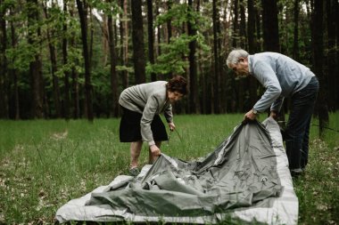Yaşlı çift tatil zevk ve çadır kuruyor. Yaz tatilini doğada geçiren yetişkinler çadır kurarlar. Yaşlılar kamp ve çadır montaj