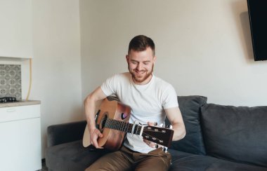 Klasik gitar çalan adam. Yakışıklı adam dairede müzik aleti ile rahatlatıcı. Akustik gitar çalan genç bir erkek. Müzisyen bir kanepede oturan ve gitar tutan