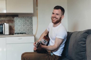 Klasik gitar çalan adam. Yakışıklı adam dairede müzik aleti ile rahatlatıcı. Akustik gitar çalan genç bir erkek. Müzisyen bir kanepede oturan ve gitar tutan