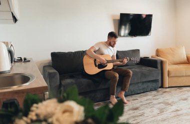 Klasik gitar çalan adam. Yakışıklı adam dairede müzik aleti ile rahatlatıcı. Akustik gitar çalan genç bir erkek. Müzisyen bir kanepede oturan ve gitar tutan