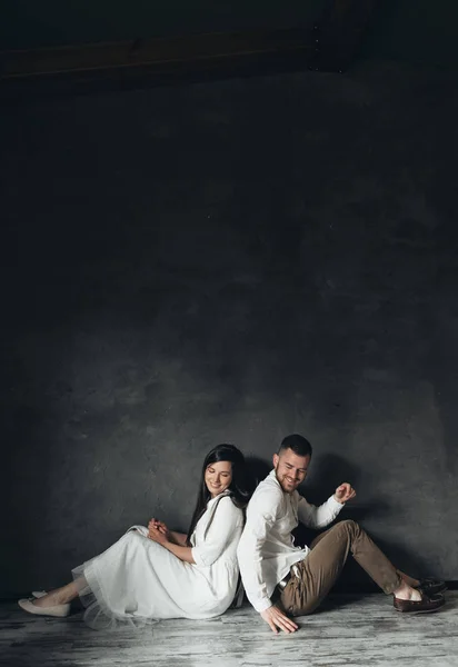 若い夫婦が家の床に座っている 黒壁の近くの白いドレスで美しいペア — ストック写真