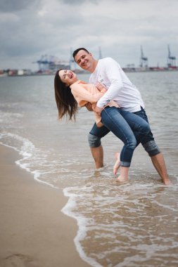 Aşık çift tatil zevk ve deniz kenarında eğlenmek. Genç mutlu aile sahilde yürüyor. Erkek ve kadın kucaklıyor ve el ele tutuşuyor. Aşıklar kumda yürür. Romantik kavram