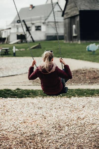 Young woman sitting on a swing in park. Pretty girl swinging on a swing against the urban landscape. Female feeling happy and healthy having fun in a sunny beautiful day