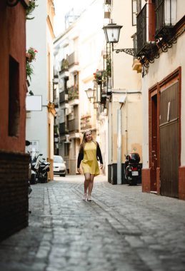 Sarı elbiseli genç güzel kadının yaz açık hava portresi. Neşeli sarışın kız eski taş evler arasında yürüyor. Portekiz'de tatil in tadını çıkarıyorum. Seyahat ve aktif yaşam tarzı konsepti