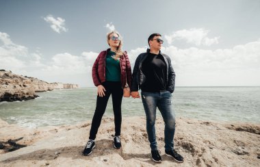 Mutlu genç çift kucaklayan ve okyanus manzaralı kayanın tepesinde el ele tutuşuyor. Kadın ve erkek uçurumun üzerinde duruyor. Portekiz'de tatil zevk siyah gözlük gülümseyen çifti