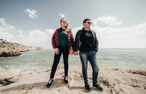 Mutlu genç çift kucaklayan ve okyanus manzaralı kayanın tepesinde el ele tutuşuyor. Kadın ve erkek uçurumun üzerinde duruyor. Portekiz'de tatil zevk siyah gözlük gülümseyen çifti