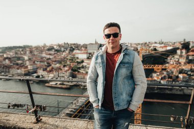 Şehrin arka planındaki köprüde kalan yakışıklı adam. Turist rıhtımda yürüyor. Genç adam Portekiz'de eski şehrin güzelliği hayran.