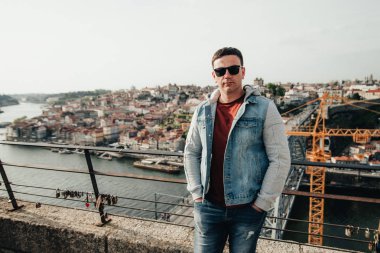 Şehrin arka planındaki köprüde kalan yakışıklı adam. Turist rıhtımda yürüyor. Genç adam Portekiz'de eski şehrin güzelliği hayran.