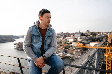Şehrin arka planındaki köprüde oturan yakışıklı adam. Turist rıhtımda yürüyor. Genç adam Portekiz'de eski şehrin güzelliği hayran.
