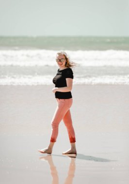 Mutlu genç kadın sahilde güneşli günlerin tadını çıkarıyor. Portre güzel kız yürüyüş ve kum ile oynarken. Okyanus kenarında poz veren gülümseyen sarışın kadın. Portekiz'de Tatil