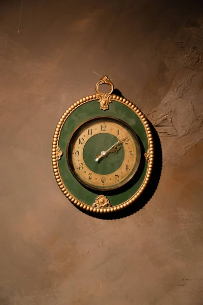 Gold vintage clock with arabic numbers. Beautiful green frame clock hanging on the brown wall. Antique round wall timepiece. Copyspace
