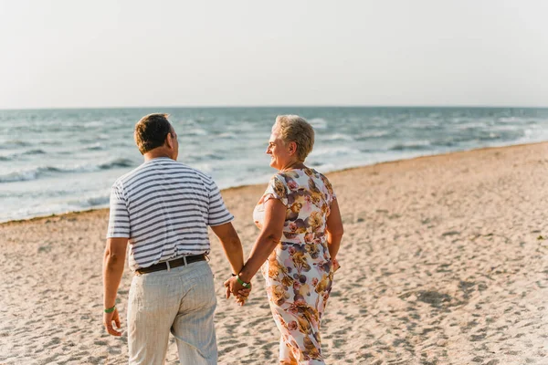 Sahilde birlikte duran romantik yetişkin çift. Olgun çiftler tatilde deniz kenarında dinlenirler. Mutlu aile yürüyüşleri ve deniz kenarında el ele tutuşmalar. Karı koca kucaklaşması. Deniz kenarında bir aşk hikayesi