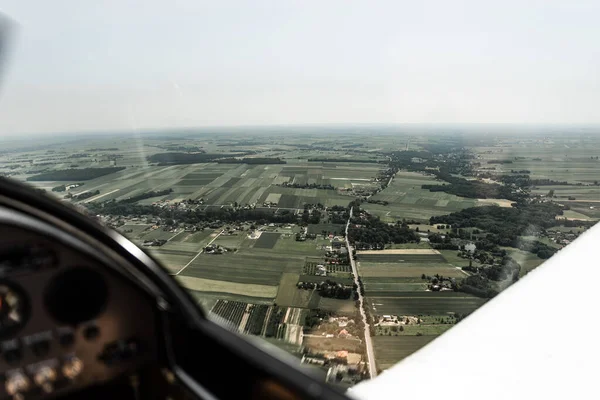 View from pilot\'s cabin. Control panel. Close up of a pilot flying airplane over the fields and village. Many buttons, navigation devices on dashboar