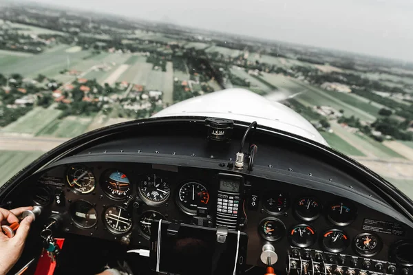 View from pilot\'s cabin. Control panel. Close up of a pilot flying airplane over the fields and village. Many buttons, navigation devices on dashboar