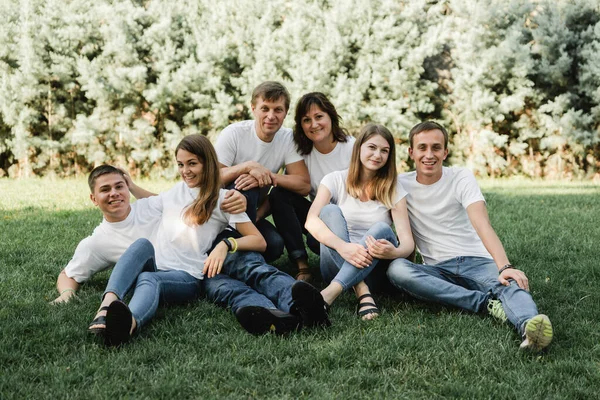 Happy family in white T-shirt and jeans sitting on the green grass. Parents with their adult children walking in the park. Family time concept