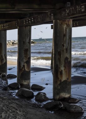 Ahşap iskelenin altından görülen bir ufukta kargo gemisi. Gdynia, Polonya