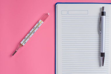 Mercury termometre ve defter bir kalem üzerinde pembe bir arka plan ile. Tehlikeli sıcaklık. Metin için yer kopyalayın