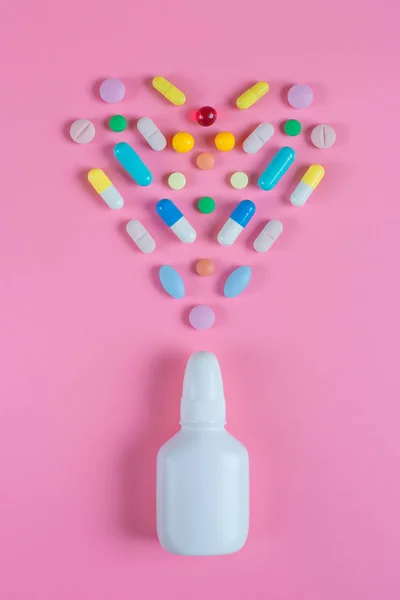White, yellow, red, blue pills, tablets and white bottle on pink background. Copy space for text