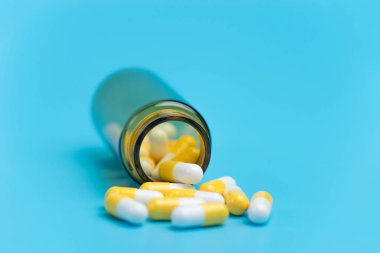 Mavi arka plan üzerinde kahverengi cam şişeden çıktı tıp beyaz ve sarı hap veya Tablet bırakın