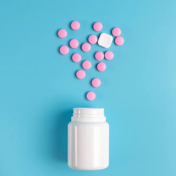 Pastillas rosadas y blancas, comprimidos en el frasco blanco sobre una espalda azul — Foto de Stock