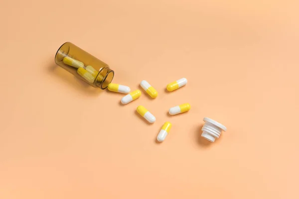 Pilules jaunes et blanches dans la bouteille en verre brun sur un bac orange — Photo