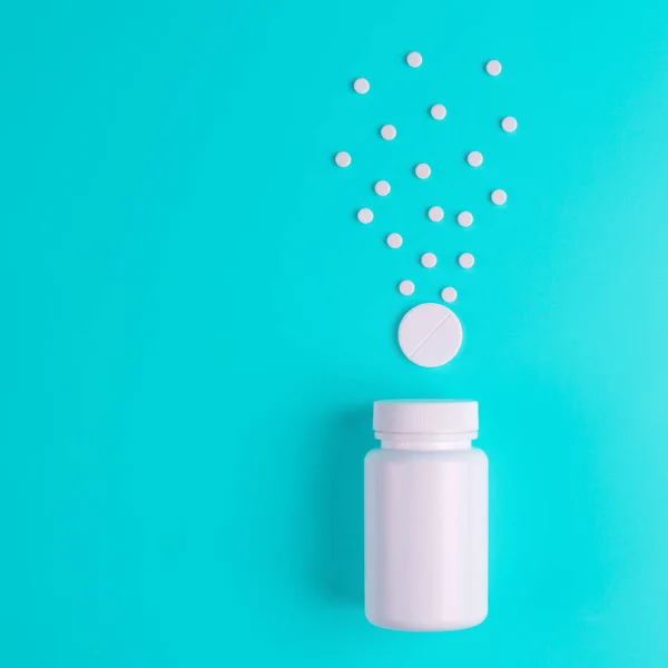 Pílulas brancas, comprimidos no frasco de vidro em um fundo azul . — Fotografia de Stock
