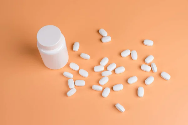 Λευκό χάπια, ταμπλέτες και άσπρο μπουκάλι σε πορτοκαλί φόντο — Φωτογραφία Αρχείου