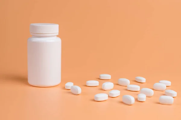 Pastillas blancas, tabletas y frasco blanco sobre fondo naranja — Foto de Stock