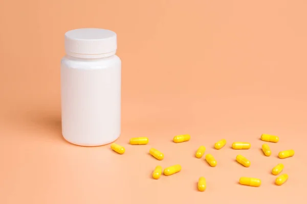 Pastillas amarillas, tabletas y frasco blanco sobre fondo naranja . — Foto de Stock