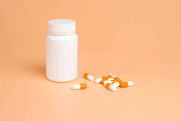 Orange and white pills, tablets and white bottle on orange backg