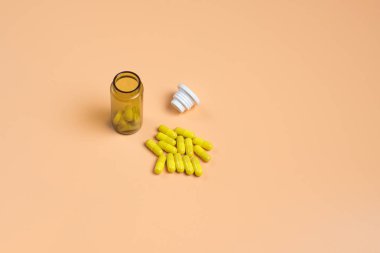 Turuncu bir arka plan üzerinde kahverengi cam şişede sarı haplar