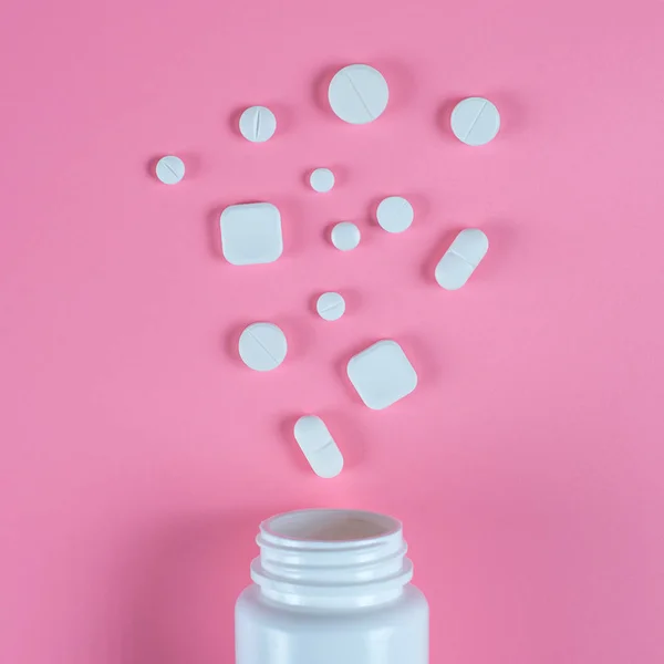 Pastillas blancas, tabletas y frasco blanco sobre fondo rosa — Foto de Stock