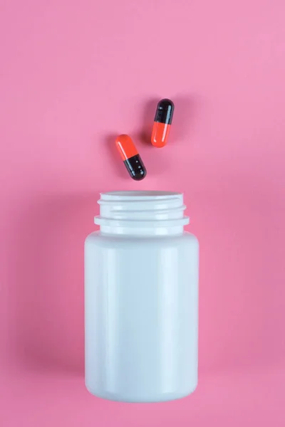 Pastillas naranjas y negras, tabletas y frasco blanco sobre fondo rosa — Foto de Stock