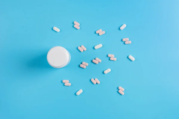 Pastillas blancas y rosadas, tabletas y frasco blanco sobre fondo azul — Foto de Stock