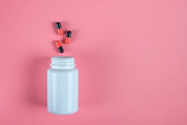 Pastillas naranjas y negras, tabletas y frasco blanco sobre fondo rosa — Foto de Stock