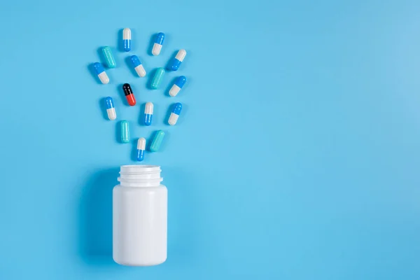 Pastillas azules y blancas, comprimidos y frasco blanco sobre fondo azul — Foto de Stock