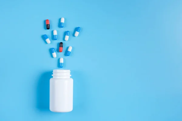 Pastillas azules y blancas, comprimidos y frasco blanco sobre fondo azul — Foto de Stock