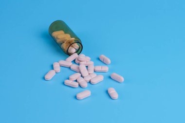Pembe haplar, mavi arka planda cam şişedeki tabletler