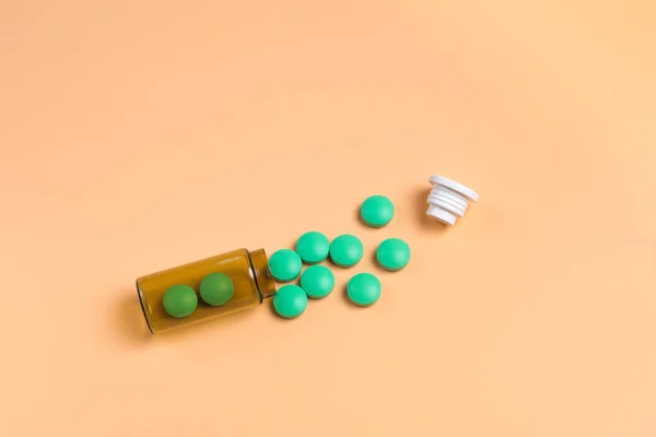 Pilules vertes dans la bouteille en verre brun sur un fond orange . — Photo