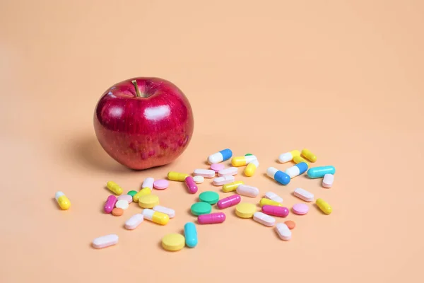 Píldoras de color y manzana sobre un fondo naranja — Foto de Stock