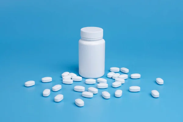 Comprimidos brancos, comprimidos e frasco branco sobre fundo azul — Fotografia de Stock